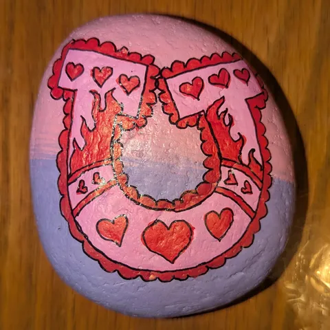 A pink and lavender stone painted with a lace-trimmed red horseshoe and small red hearts.