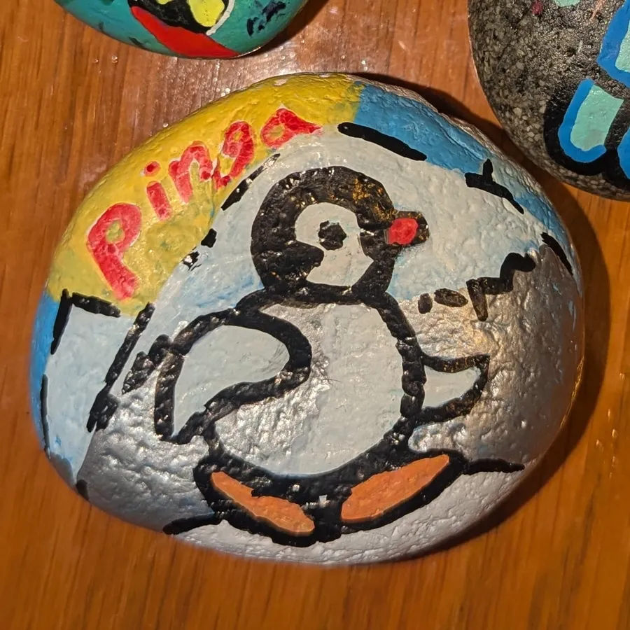 A white stone painted with Pingu the penguin and the word "Pingu" in red letters.
