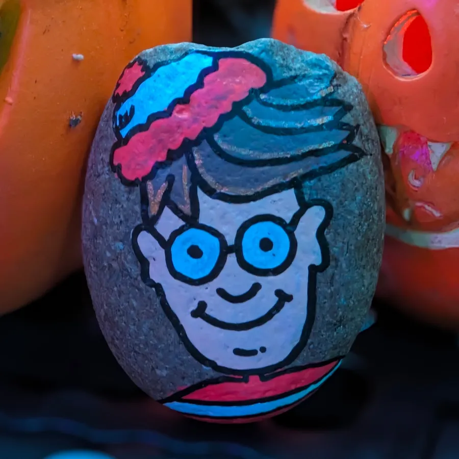 A stone painted with Waldo's smiling face, round glasses, and red and white bobble hat.